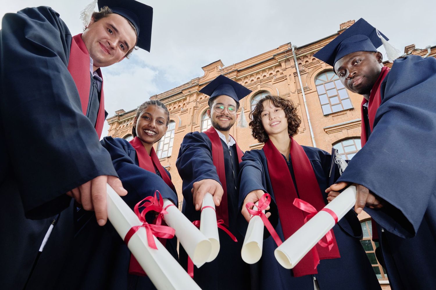 College graduates in caps and gowns celebrate their graduation by showing off their diplomas outdoors.