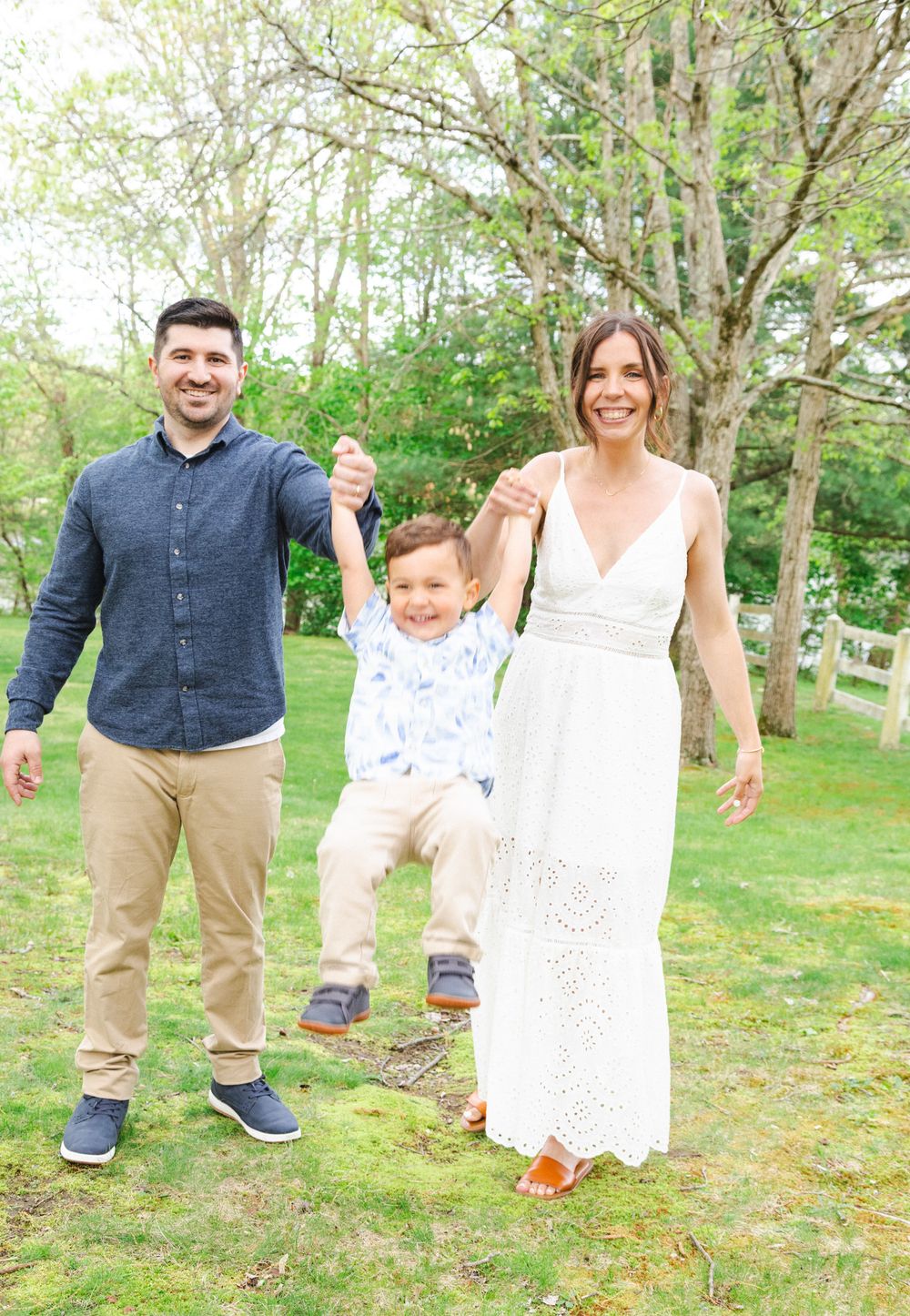 A family wearing white and denim outfits poses playfully in a green outdoor setting during a photo session.