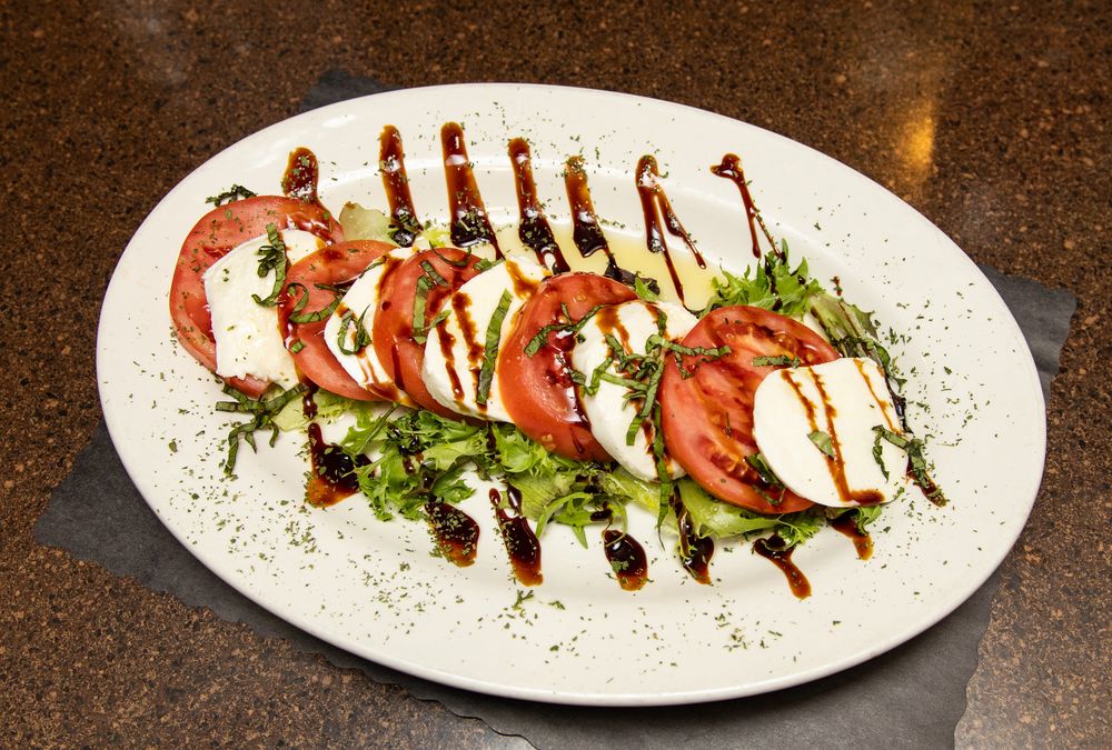 Caprese salad with fresh tomatoes, mozzarella, arugula, and balsamic glaze drizzle on a white oval plate.