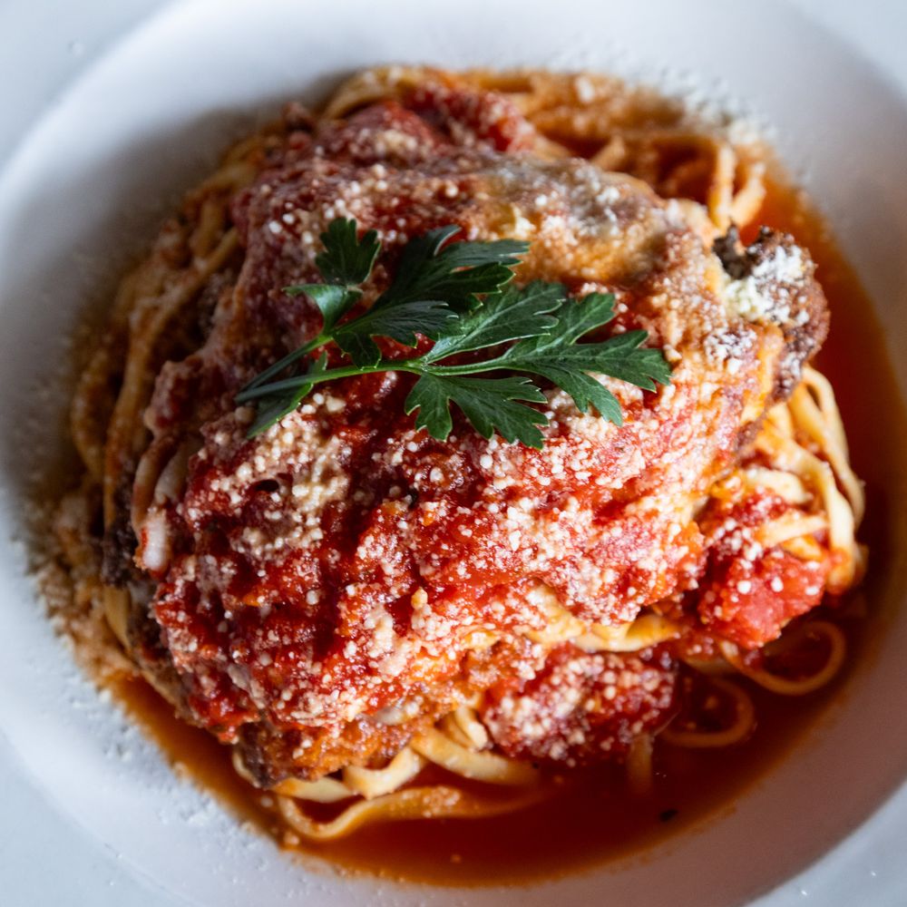 Spaghetti with meatballs in rich tomato sauce, topped with Parmesan and fresh parsley in a white bowl.