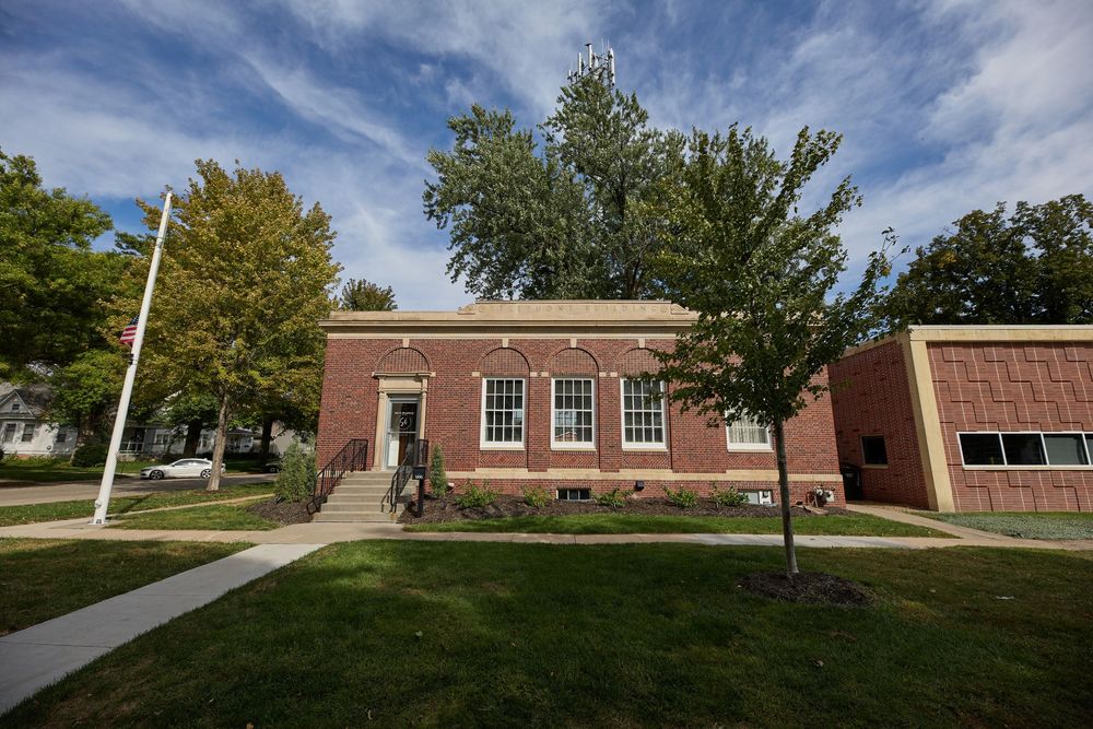 Exterior view of brick school building with walkways under blue sky and autumn trees.