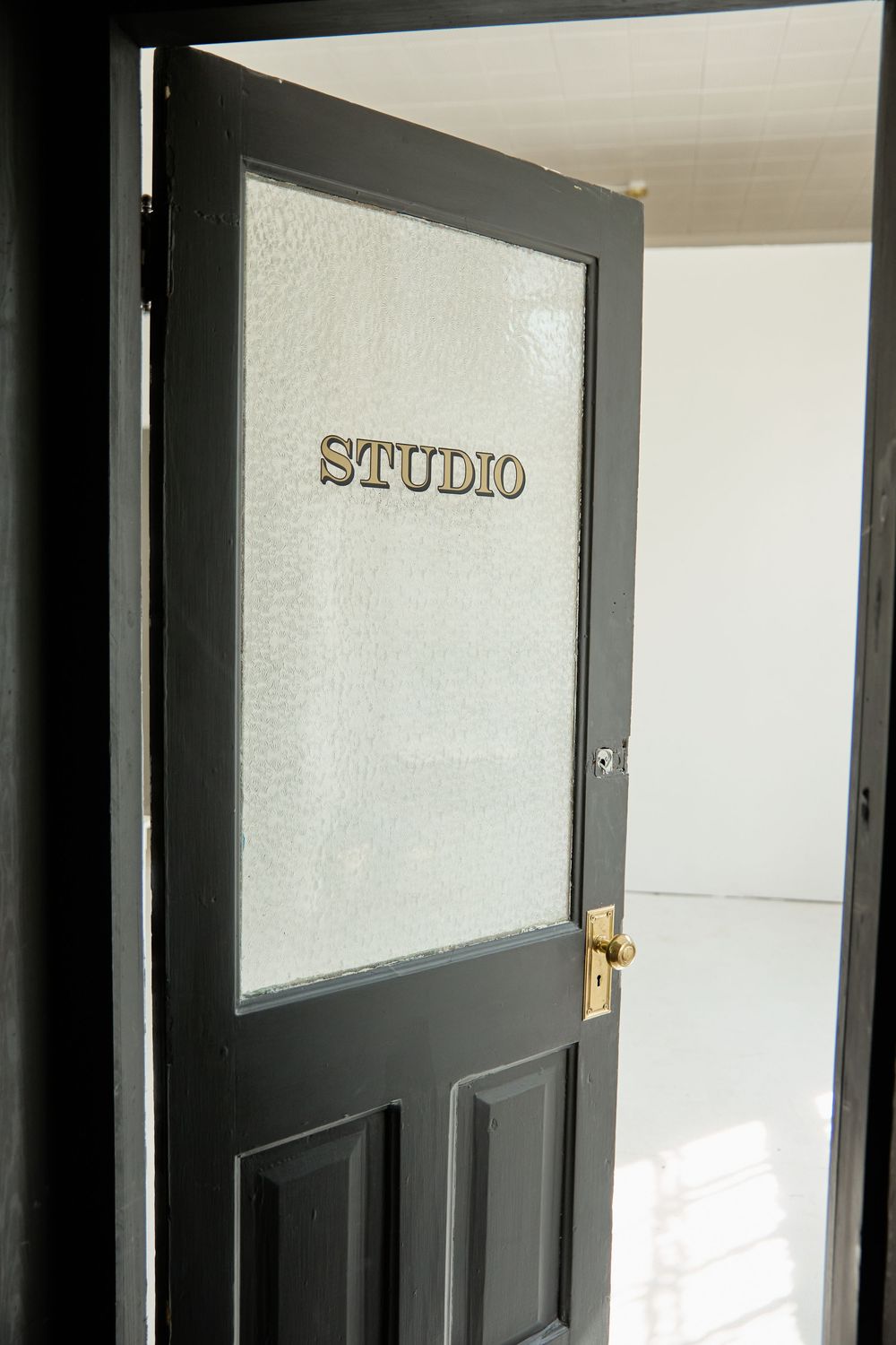 A black door with frosted glass panel and gold 'STUDIO' lettering mounted on it.