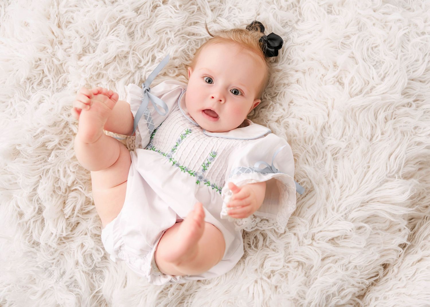 Baby lying on white textured rug in natural light during photo session.