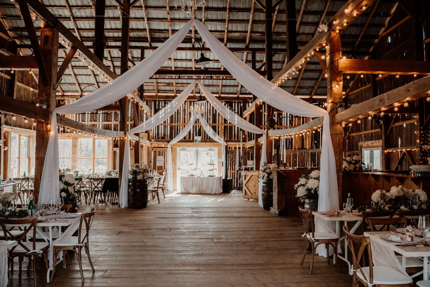 North Bay barn wedding venue draped with interior with white draping, string lights, and wooden floors creating a romantic atmosphere.