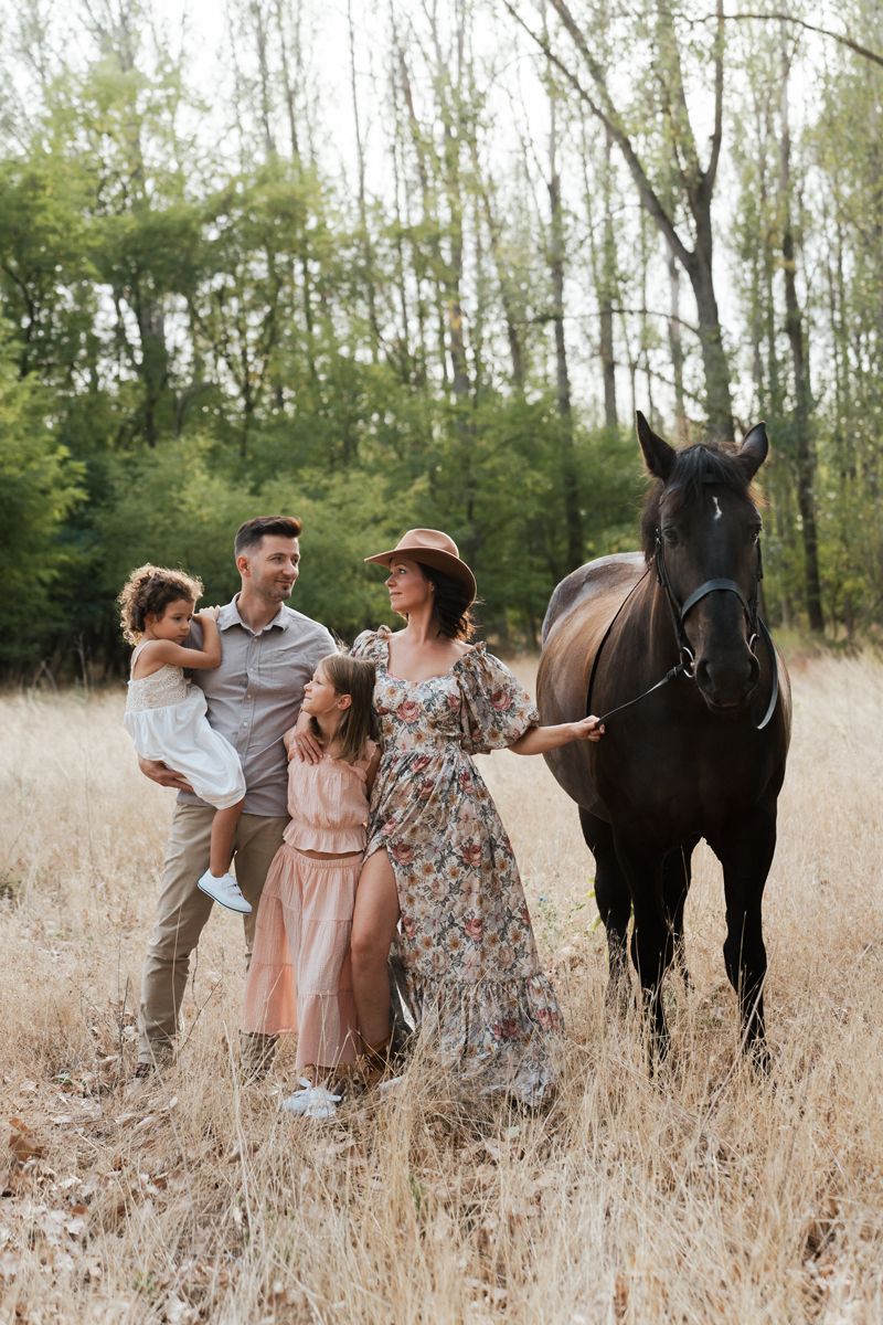 Family stands in a golden field of tall grass with a dark horse on a sunny autumn day during family photoshoot in the Hills Sydney