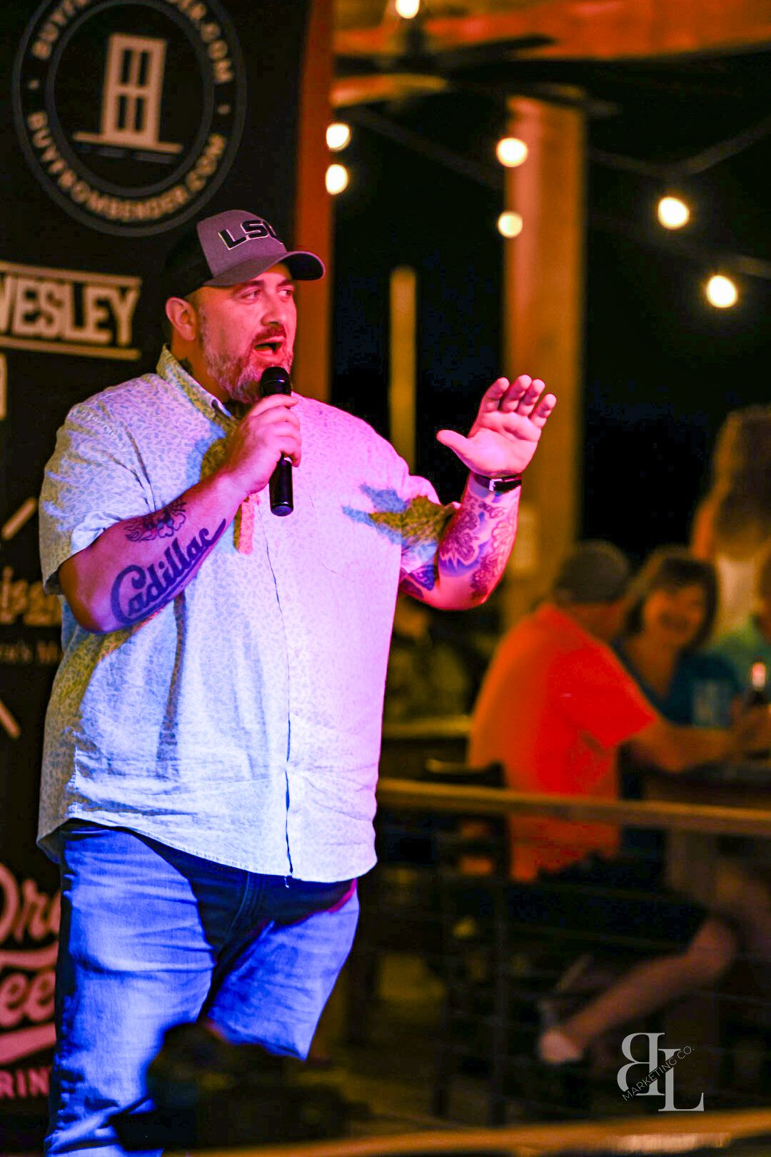 Country music performer passionately singing on stage at a dimly lit venue with string lights in the background.