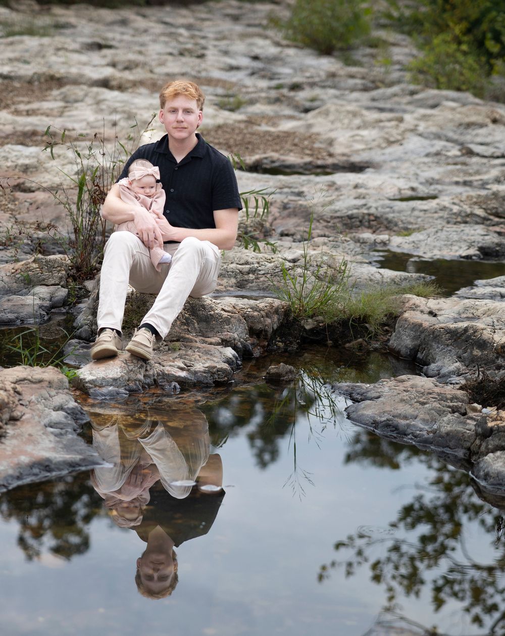 A serene scene with people sitting on rocky terrain beside a reflective pool of water in a natural setting.