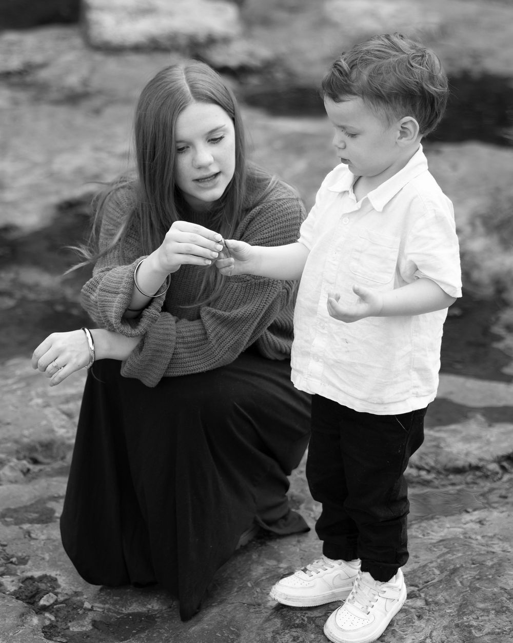 Black and white portrait of parent and child sharing a moment on rocky terrain.