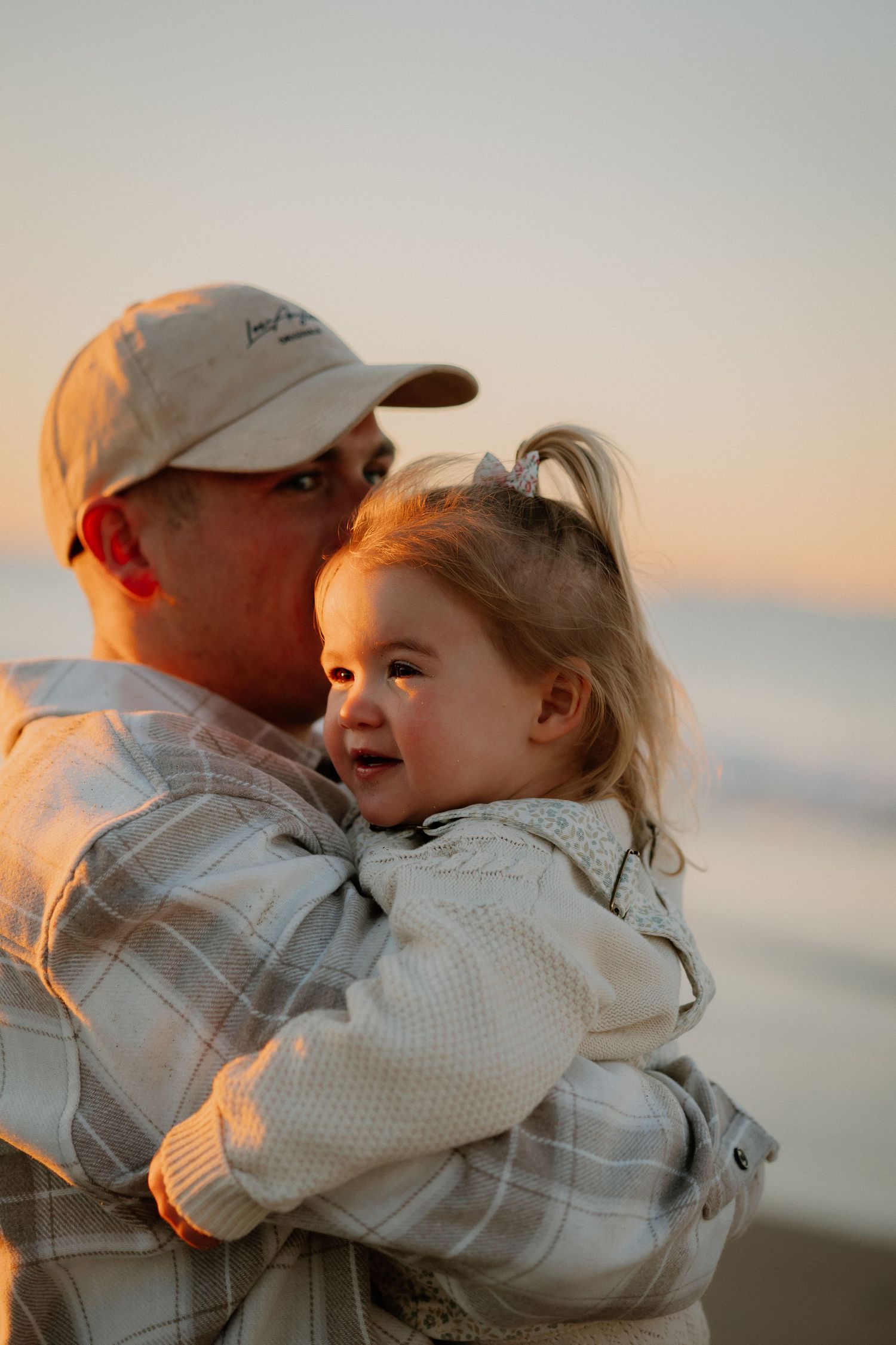 A tender moment captured at sunset by the ocean as warm golden light illuminates their faces.