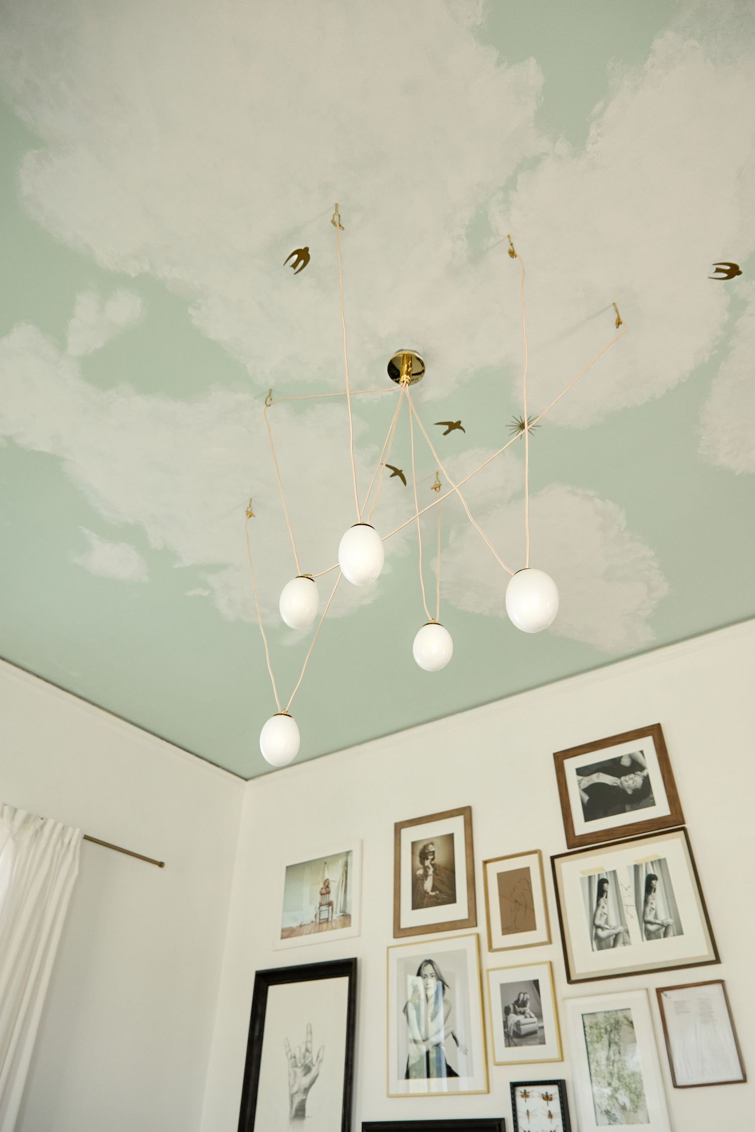 Art gallery wall with pendant lights hanging from a mint green ceiling and multiple framed photographs.