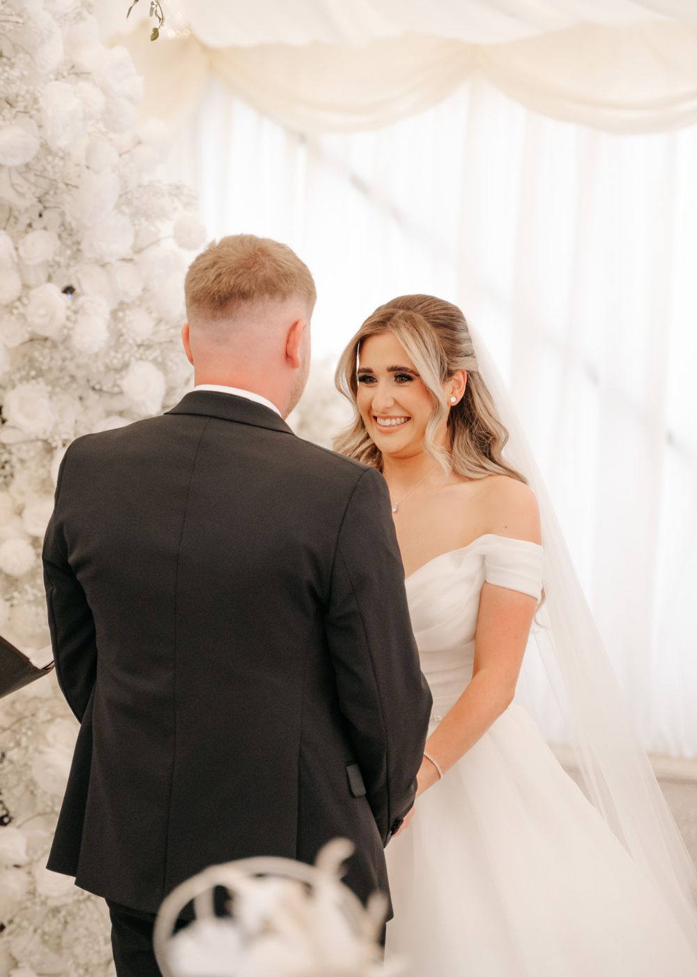 Intimate wedding moment captured under white floral arch during ceremony.