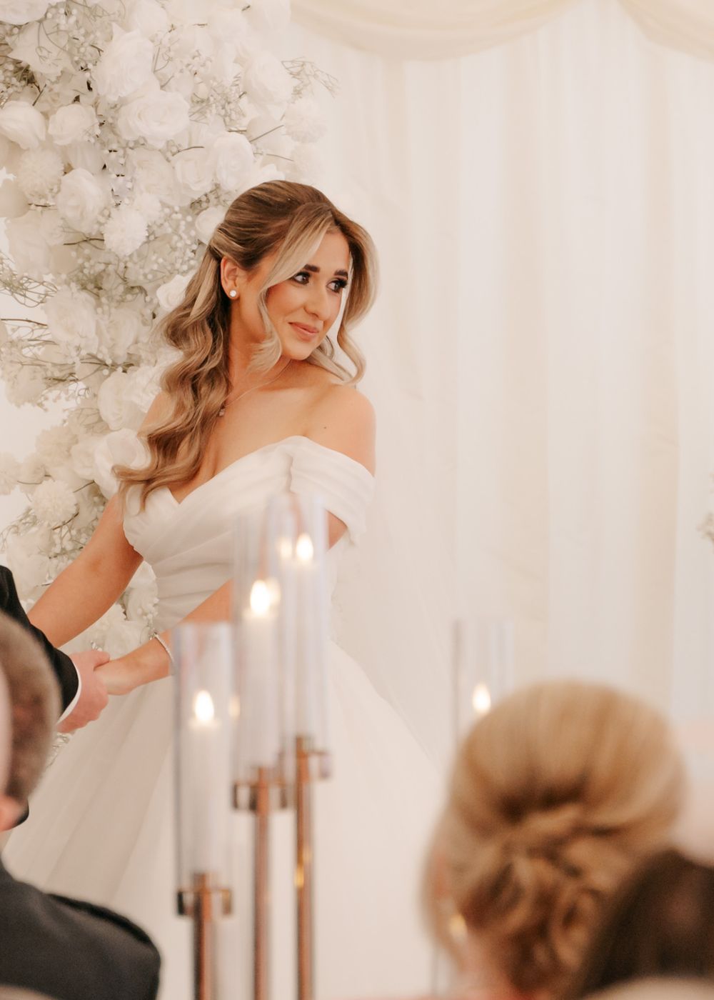 Elegant bridal portrait under white floral arch with soft lighting and romantic atmosphere.