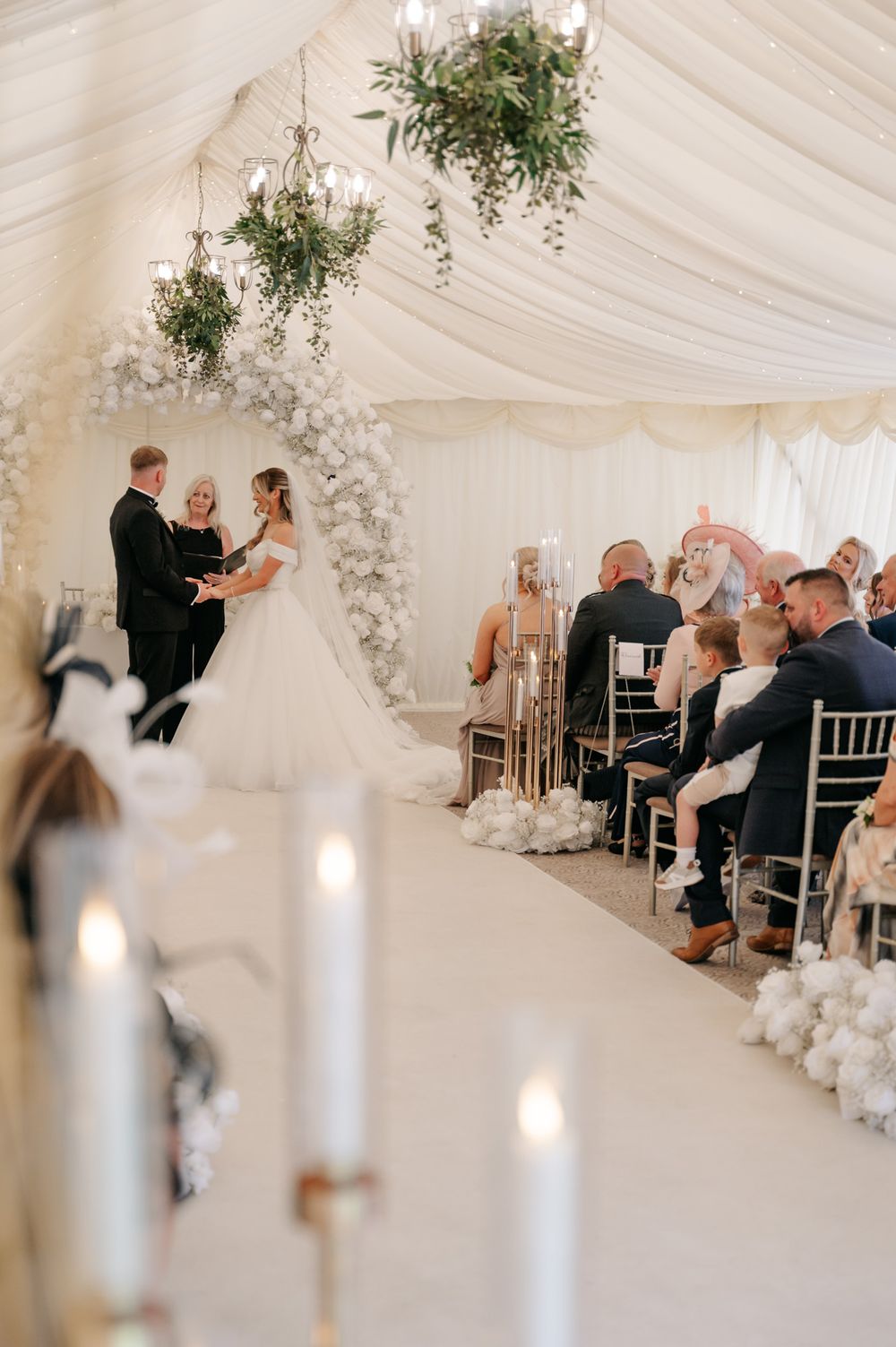 White wedding reception tent decorated with elegant floral archway and draped fabric ceiling.