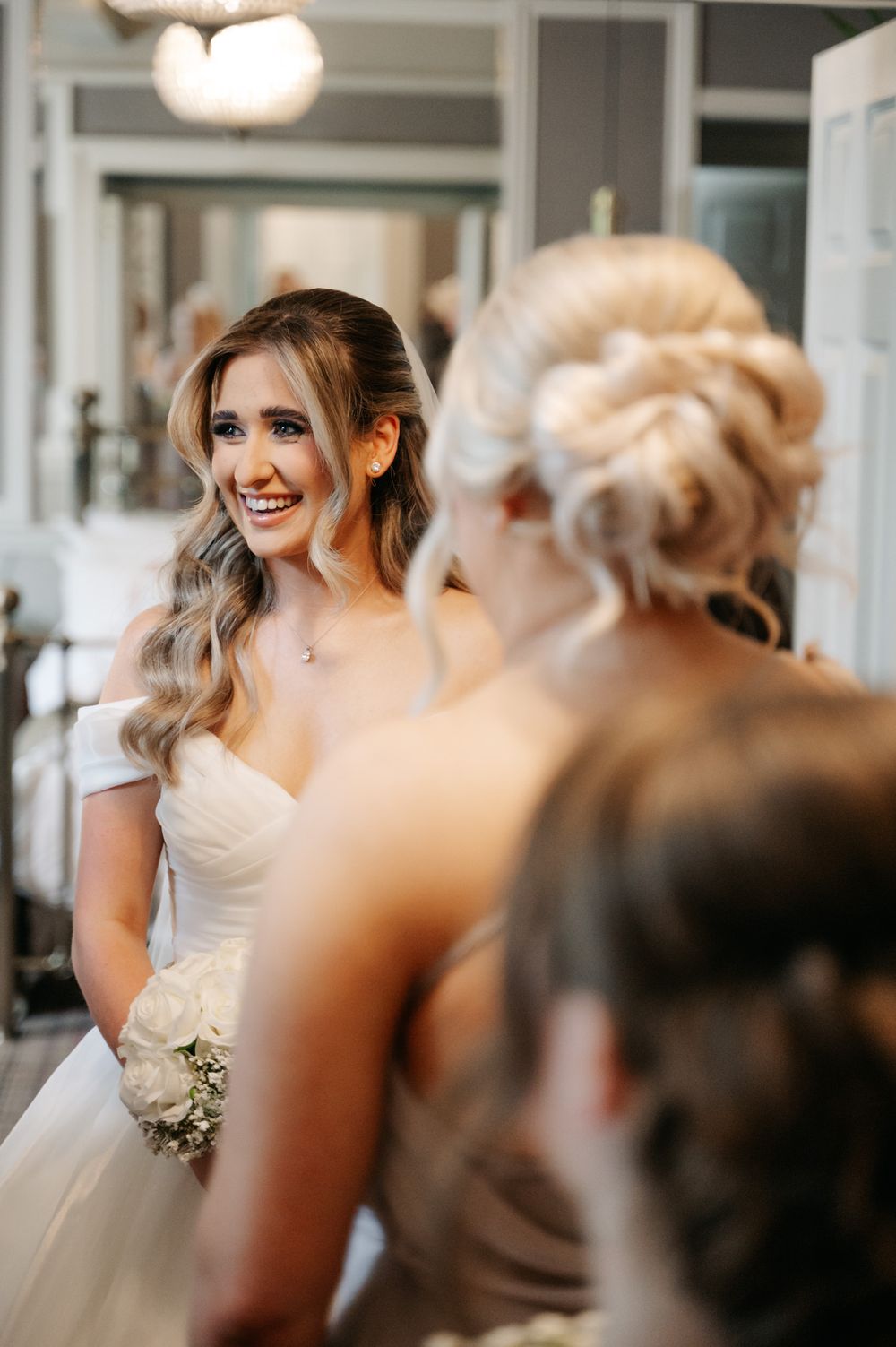 A radiant bride in a white gown shares a joyful moment during wedding preparations.