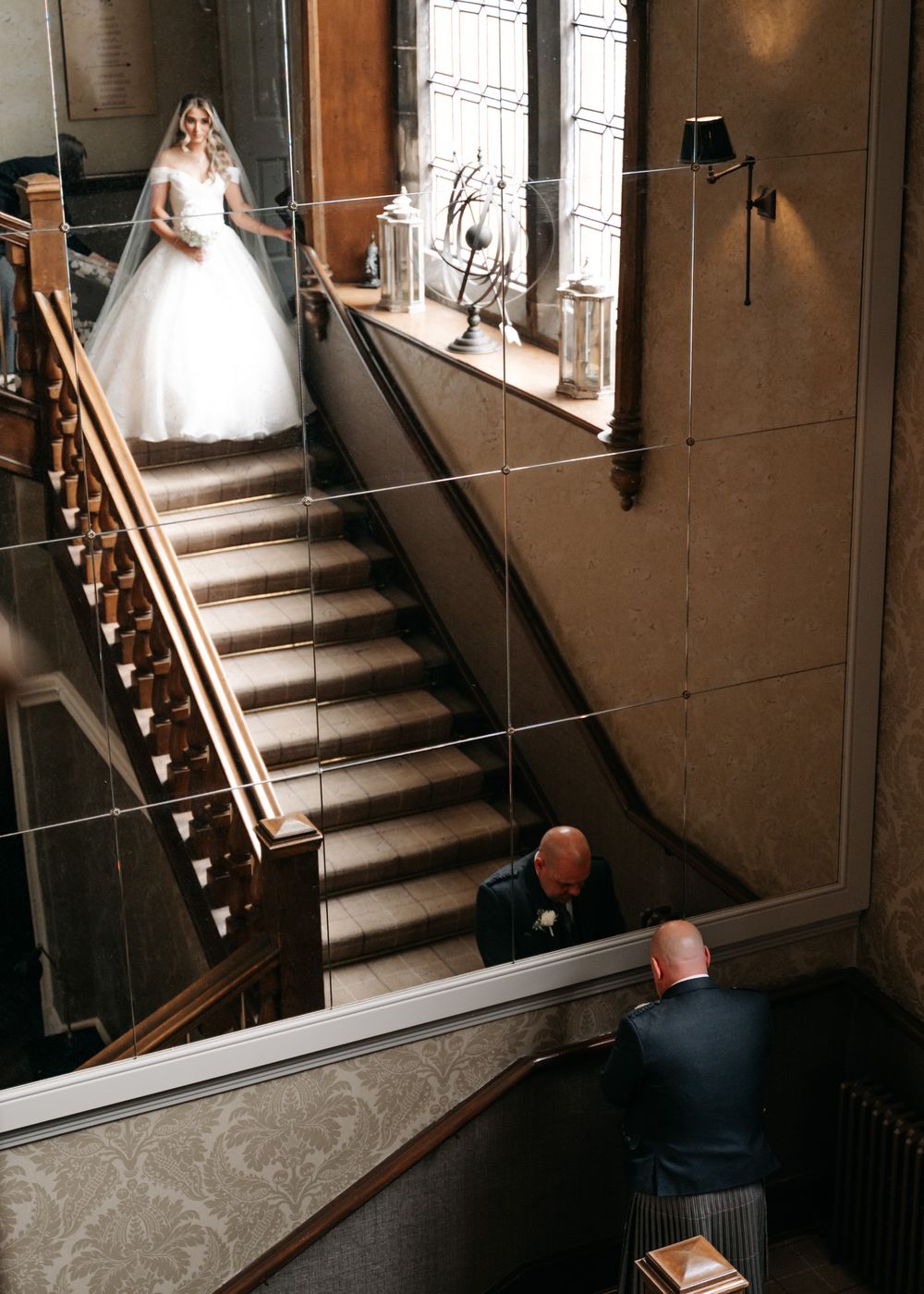 A bride in a flowing white gown descends an elegant staircase while others watch from below.