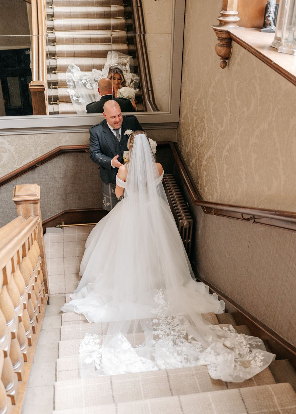 An emotional wedding moment captured on an elegant staircase with flowing bridal gown train. Father and daughter moment in Lanarkshire.