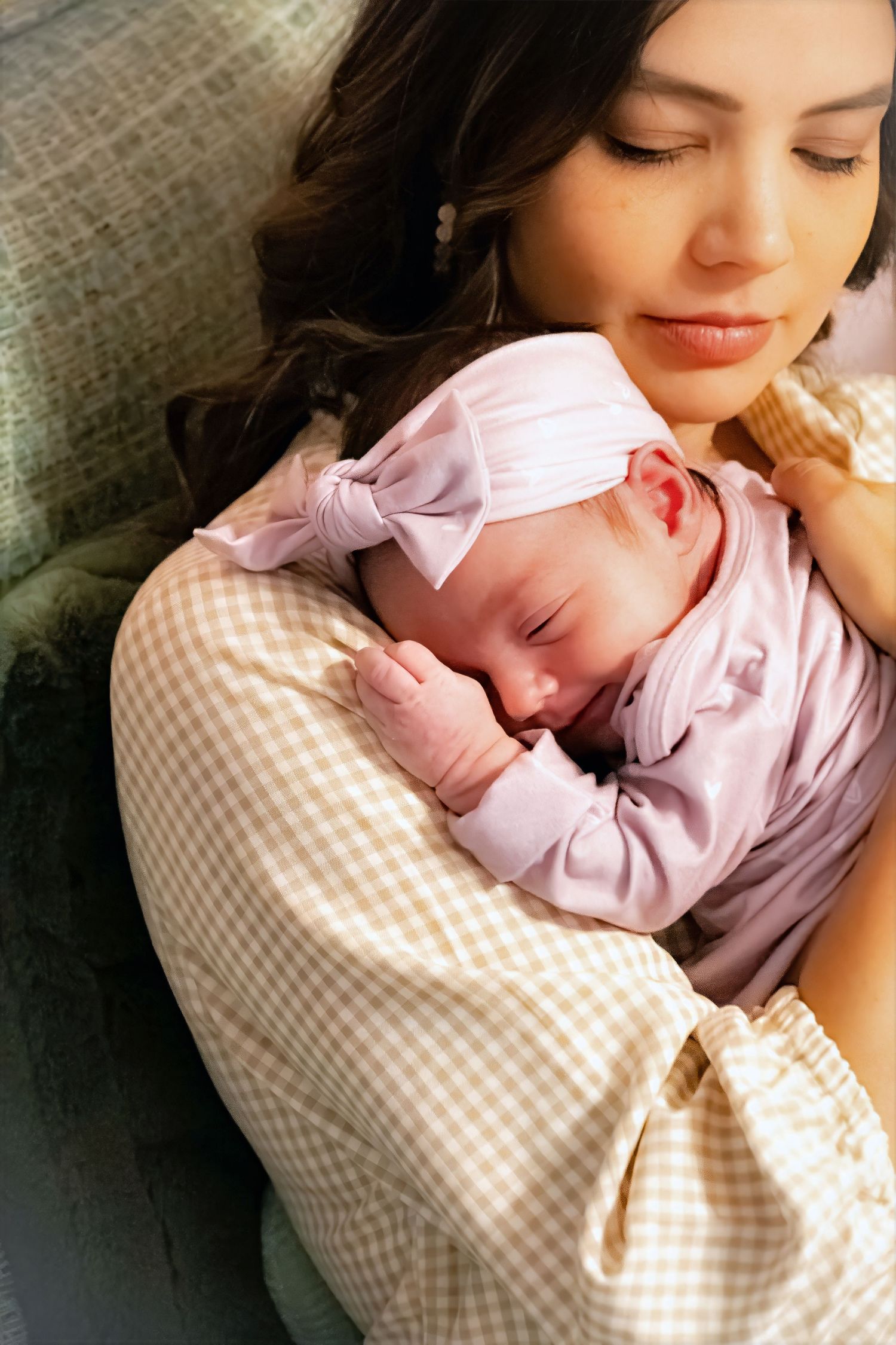 A tender moment showing a parent cradling a sleeping baby wearing a pink outfit against a gingham patterned background.