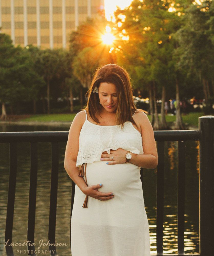A person in a white dress stands on a waterfront deck at Lake Eola Park, Orlando Maternity Photography, Sanford Maternity Photography