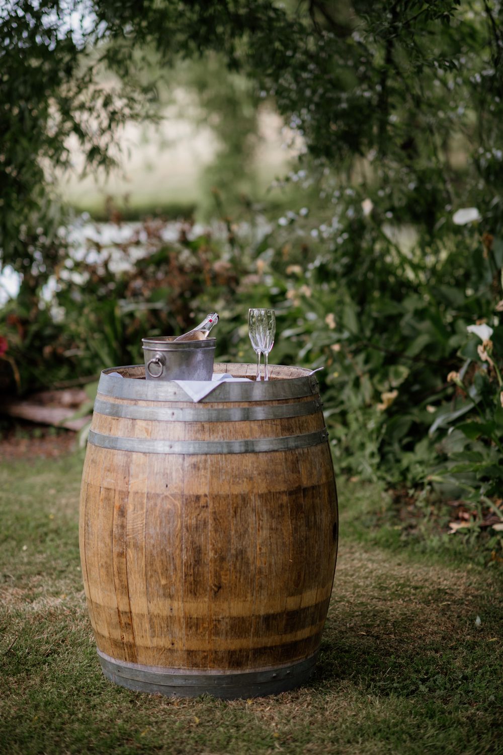 Champagne in a champagne bucket with two glasses on a rustic wine barrel by the pond at Parehua Resort by August & Vine