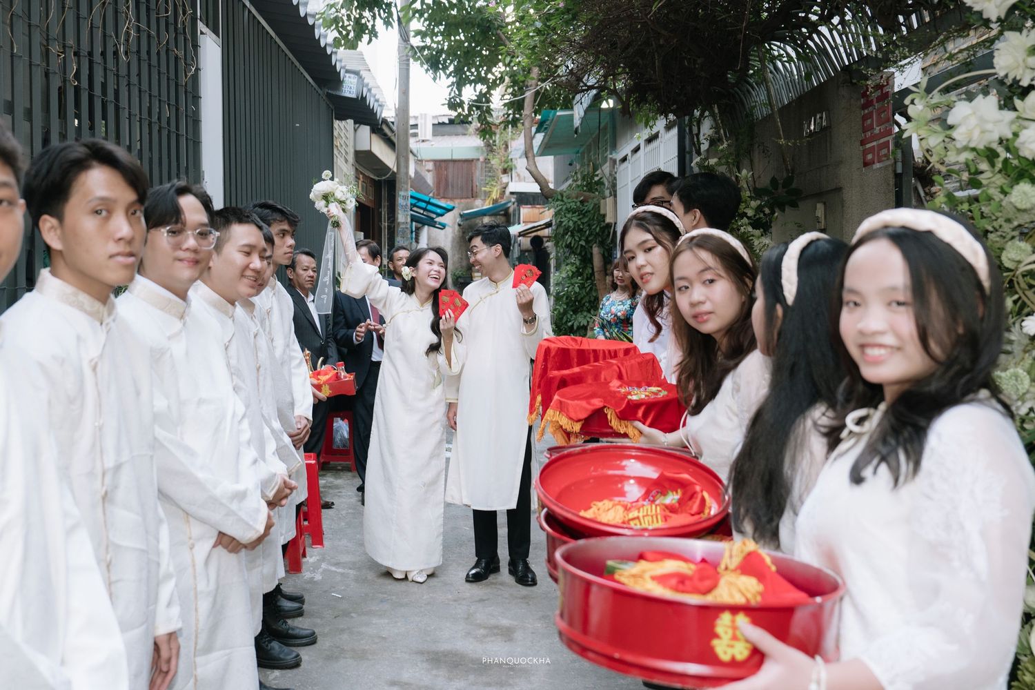 Traditional Vietnamese wedding ceremony with guests dressed in white ao dai carrying red lacquer trays with gifts.