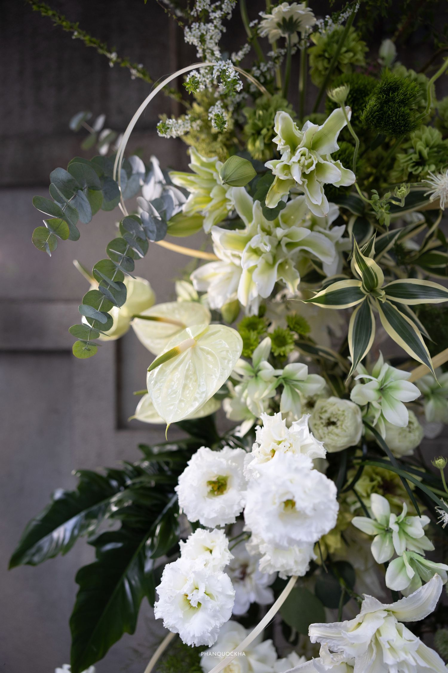 Elegant white and green floral wedding arrangement featuring anthuriums, roses, and eucalyptus leaves.
