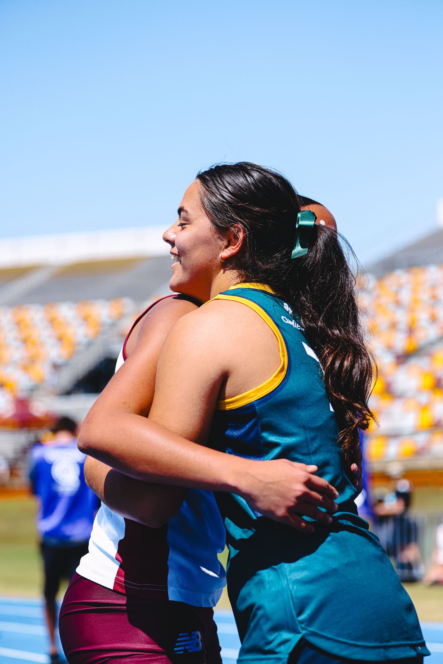 Athletes competing in a relay race pass the baton during a track and field event at a stadium with colorful seats.
