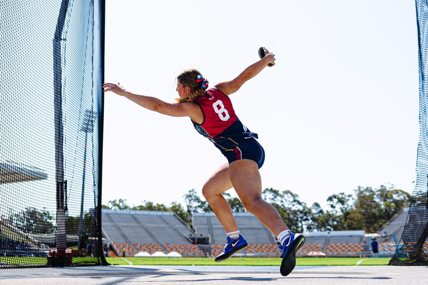 Athletes perform stretching exercises on an outdoor track during a sunny day workout session.