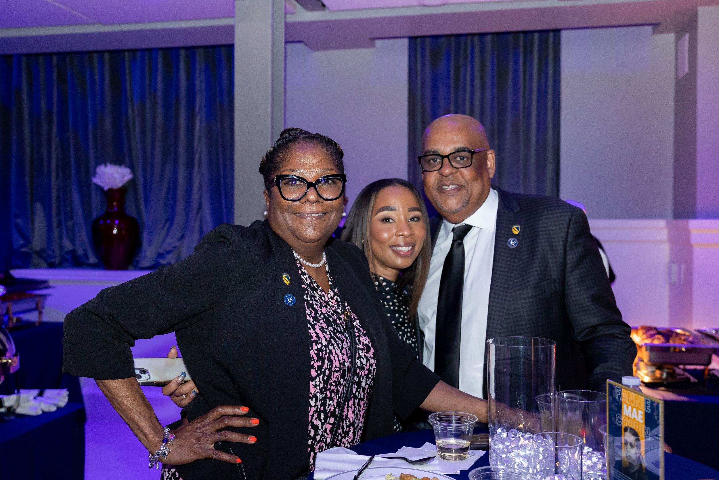 Three people posing together at a blue-lit evening gala event.