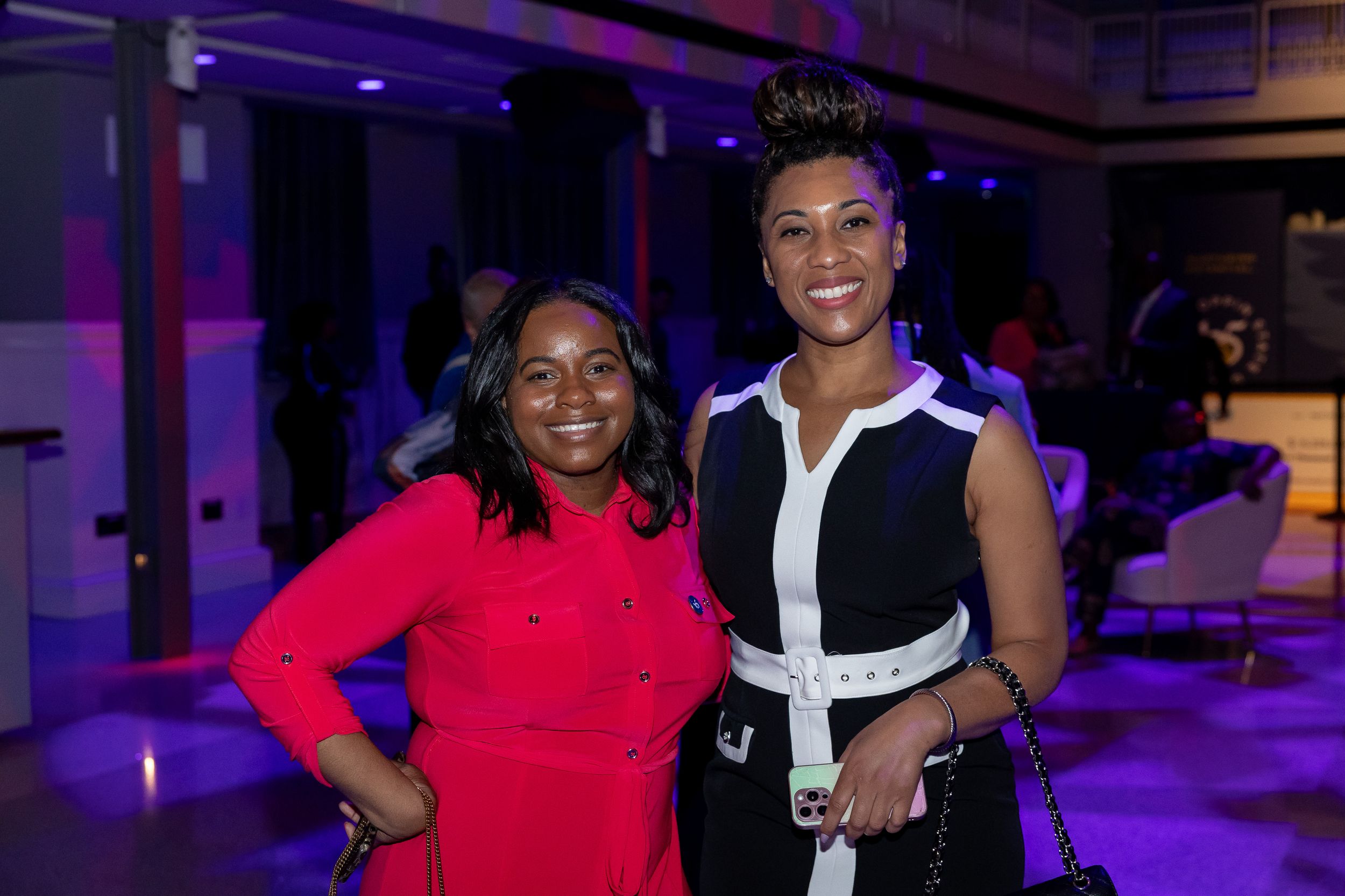 Two women posing together at a blue-lit evening event in colorful outfits.