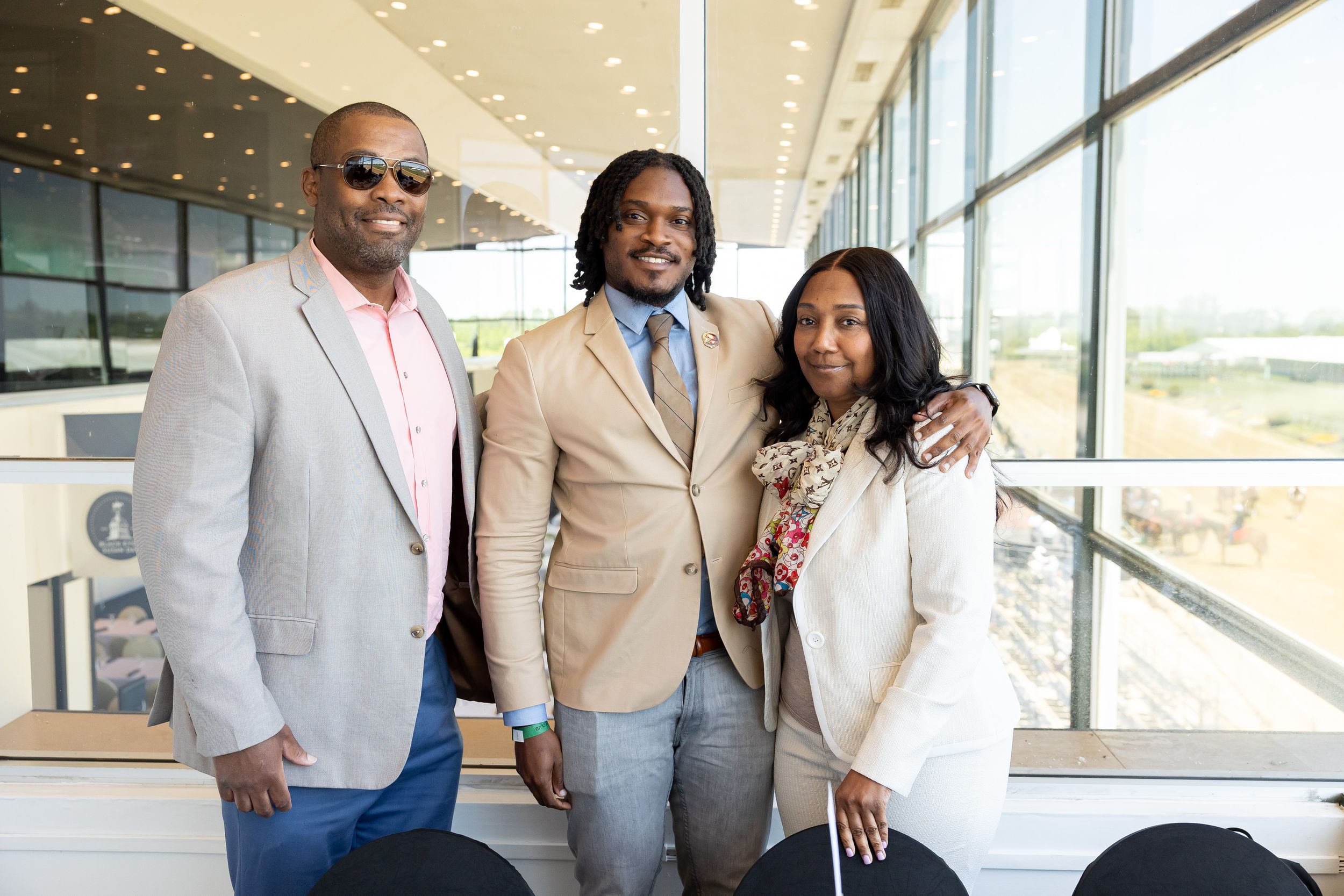 Three people smiling and posing together near large windows in a bright, modern event venue.