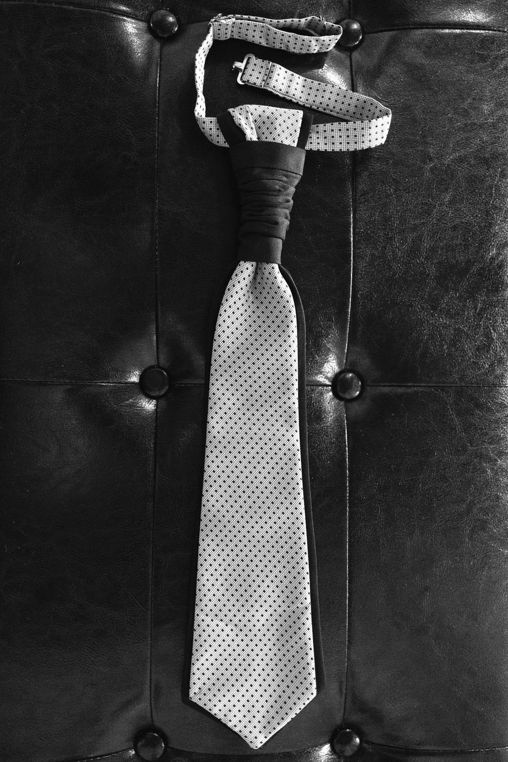 A polka dot necktie is displayed on dark leather upholstery with tufted buttons.