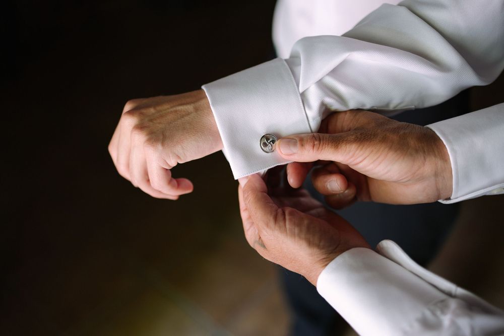 Close up view of hands adjusting a white dress shirt cuff button against dark background.