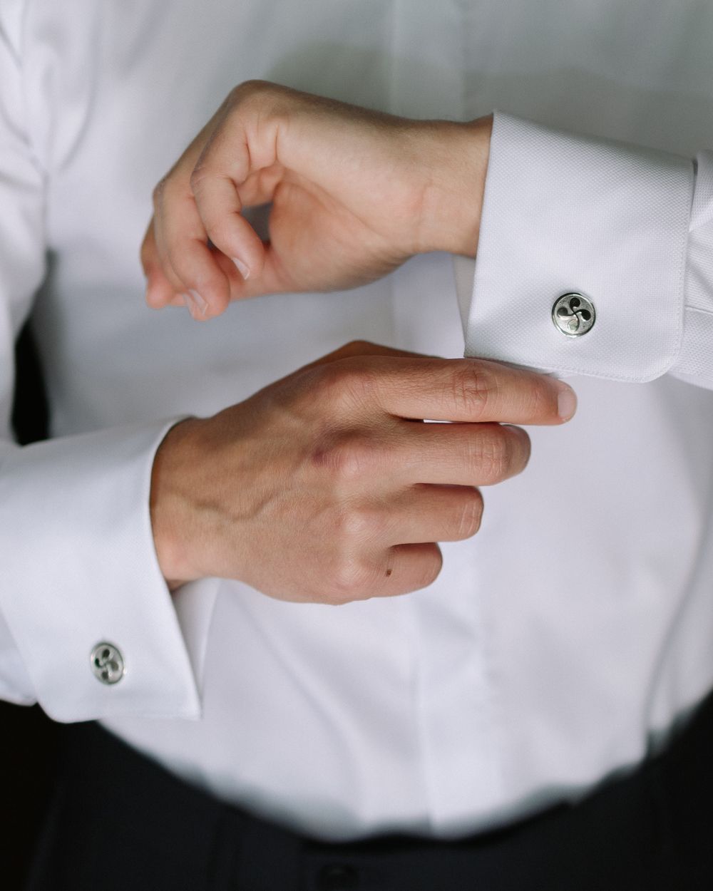Close-up view of hands adjusting formal white shirt cuffs with silver cufflinks.