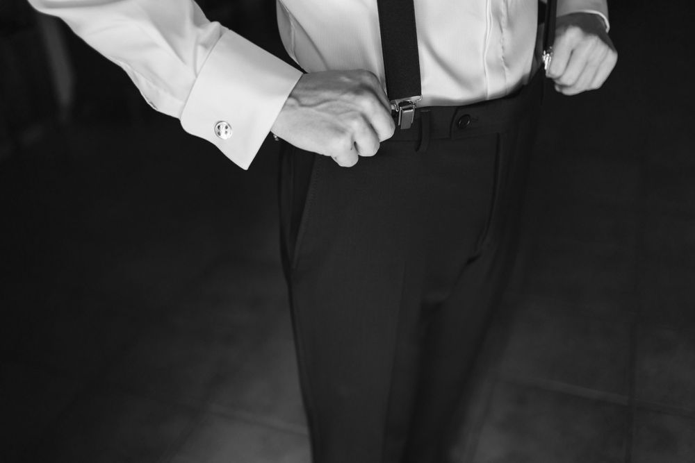 A black and white image shows hands adjusting formal attire with crisp white dress shirt cuffs visible.