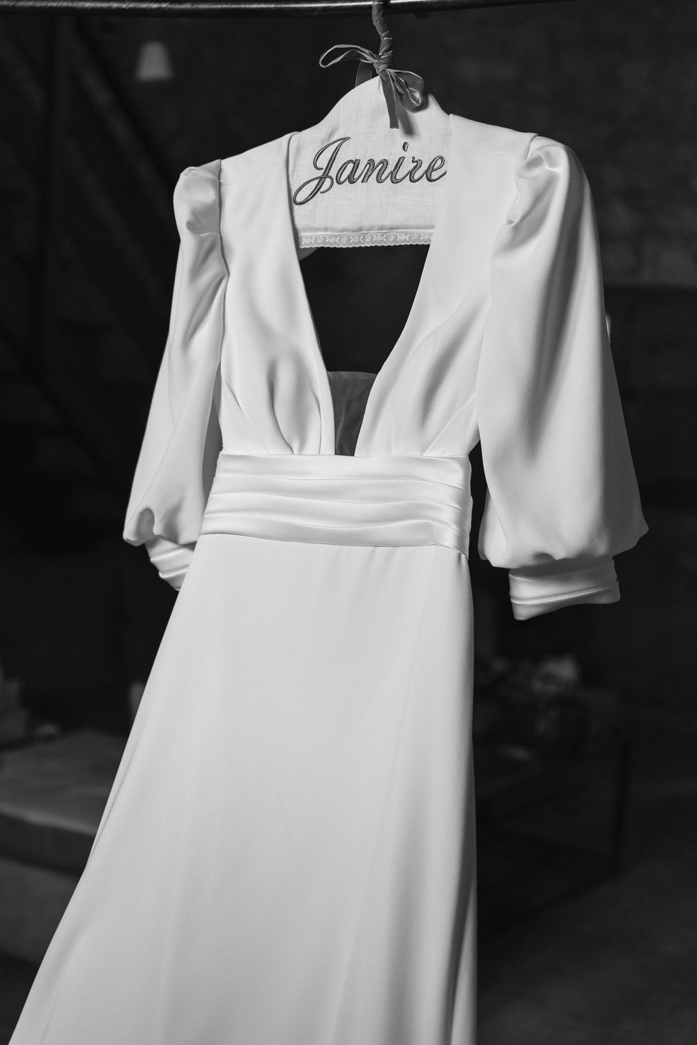 A classic white wedding dress with dramatic puff sleeves and plunging neckline hangs on a personalized hanger.