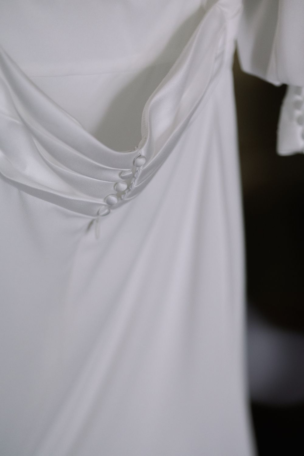 Close-up detail of delicate buttons on white fabric garment with soft draping and elegant texture.