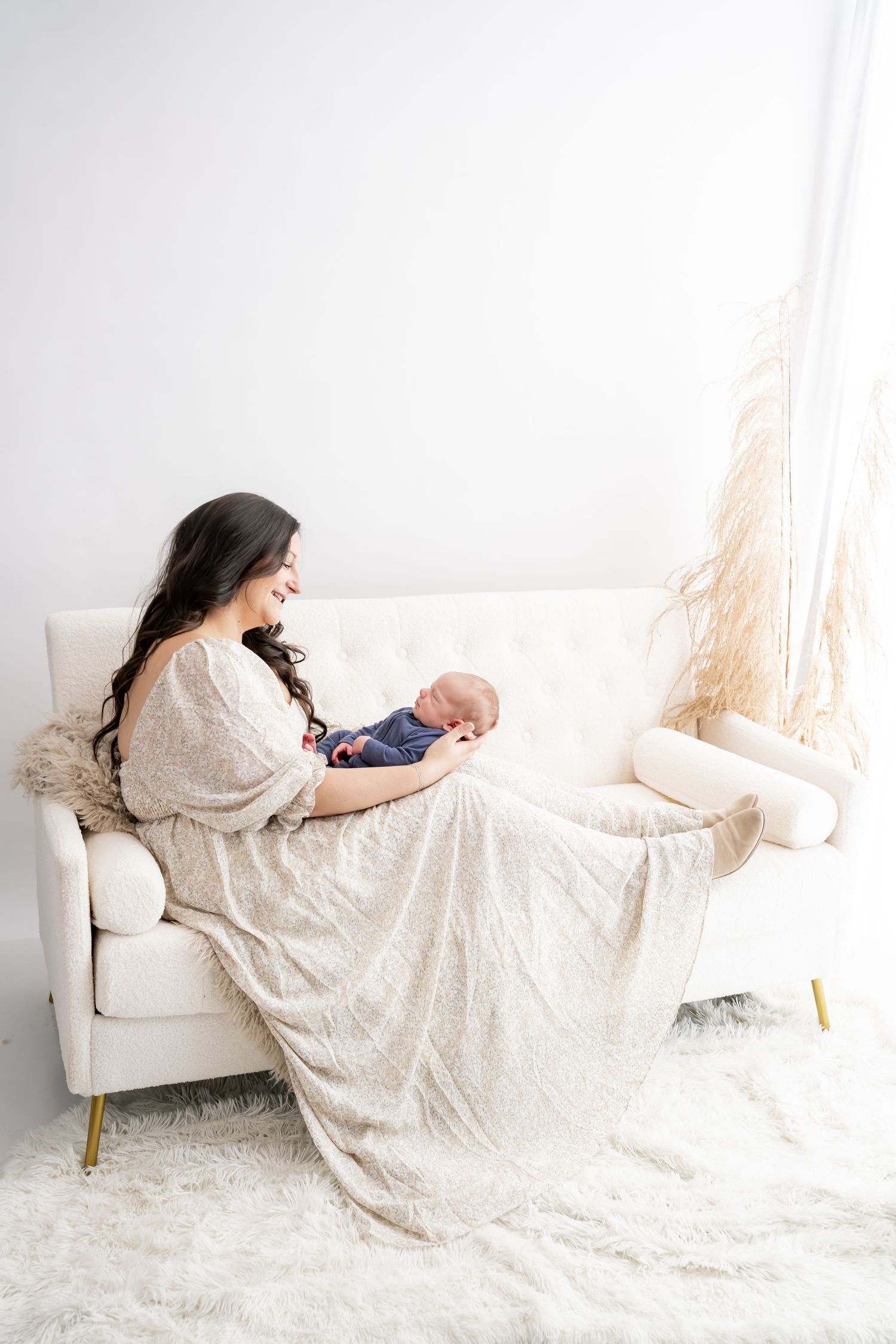 Woman in flowy white lace dress lying gracefully on white couch in minimalist studio setting.