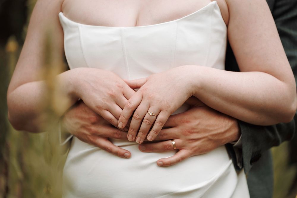 Close-up of bride and groom's hands showing wedding rings as groom embraces bride.
