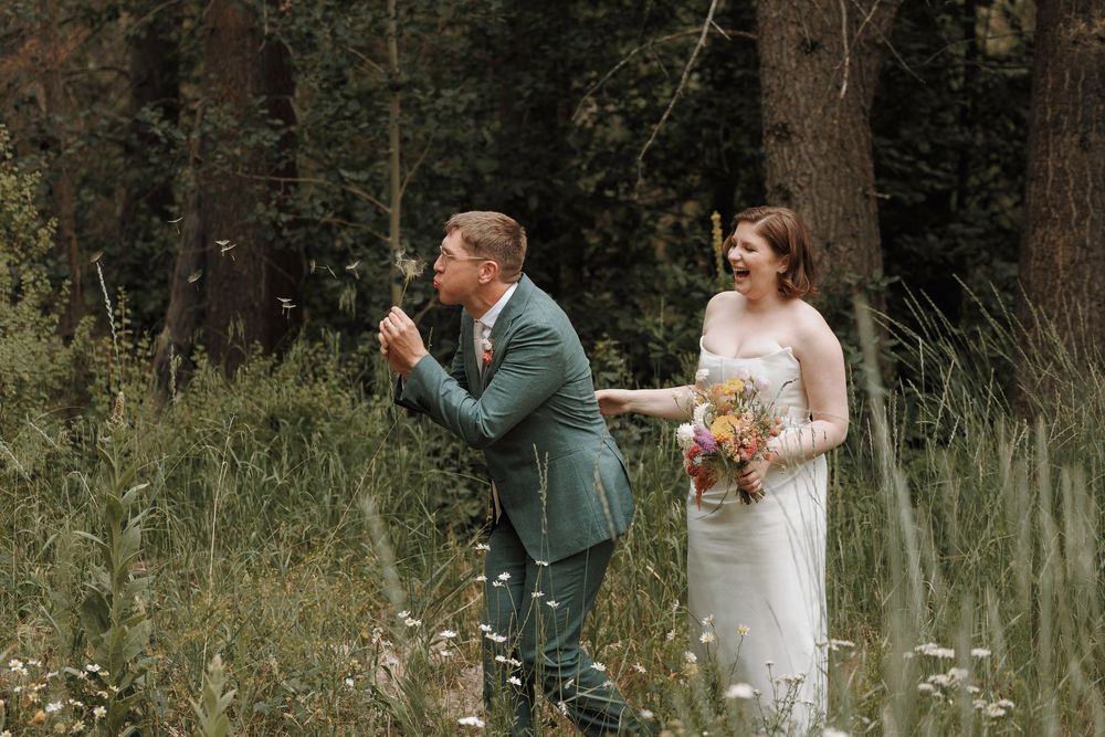 Groom kneeling in wildflower meadow reacting with joy during first look with bride holding colorful bouquet.