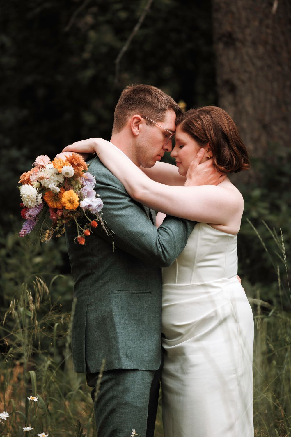 Bride and groom share intimate forehead touch embrace in lush green forest setting on wedding day.