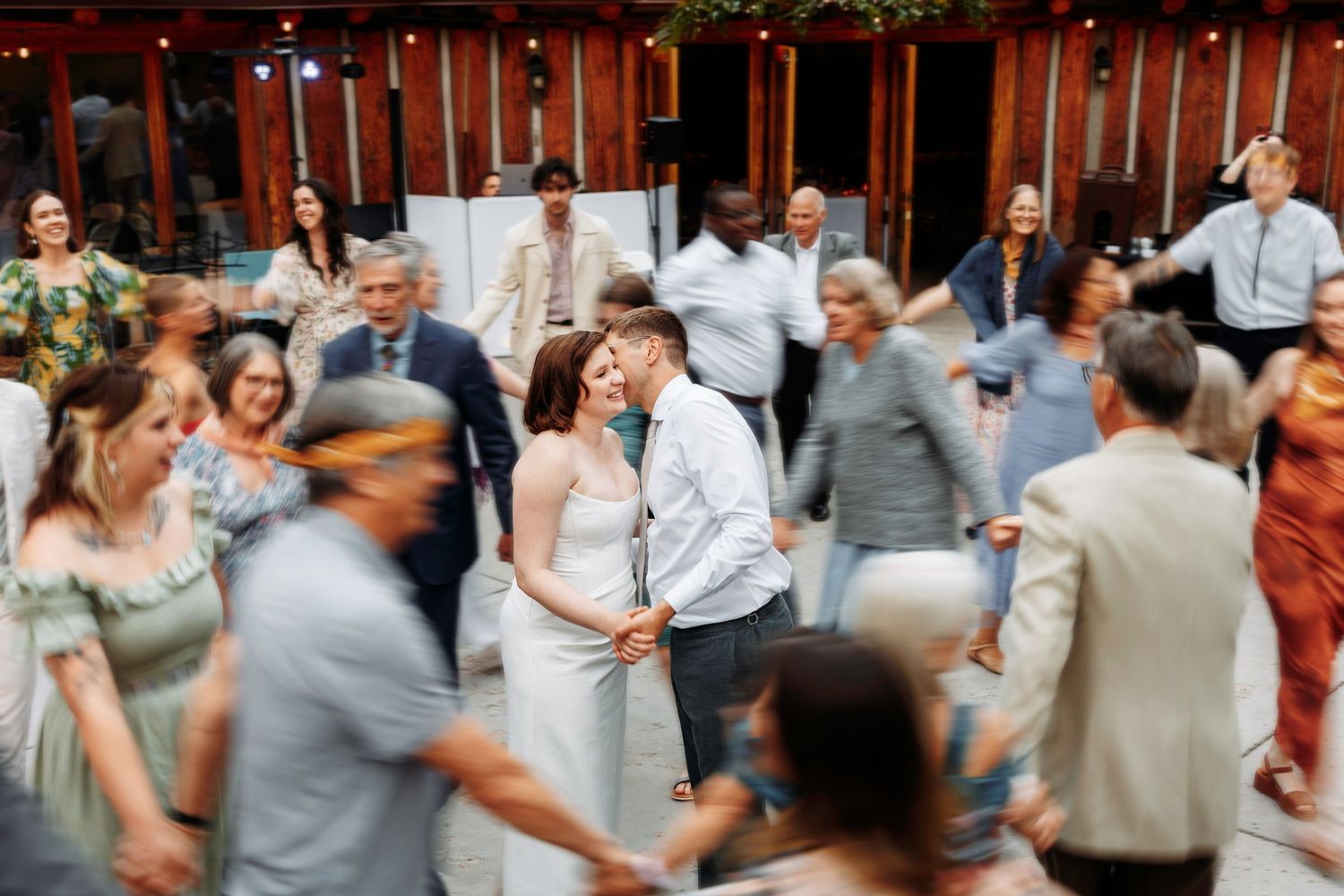 Bride and groom sharing a kiss on the dance floor surrounded by dancing wedding guests.