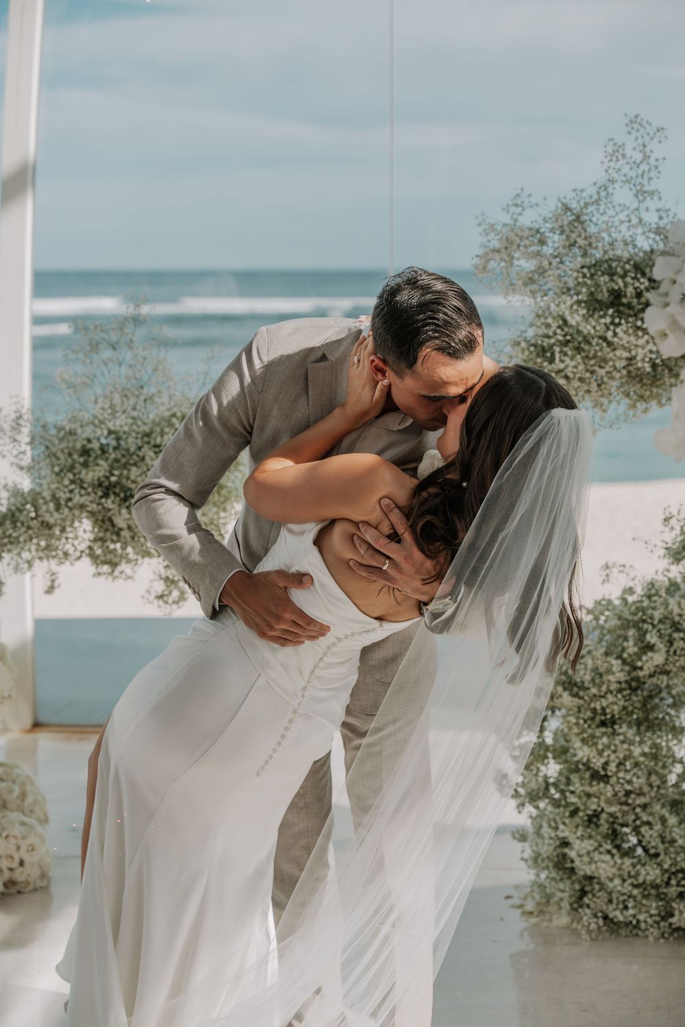 Romantic wedding couple sharing an intimate dip kiss against an oceanfront backdrop.