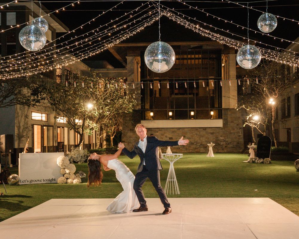 Wedding dancer dip beneath glowing disco balls and string lights on an elegant outdoor dance floor at night.