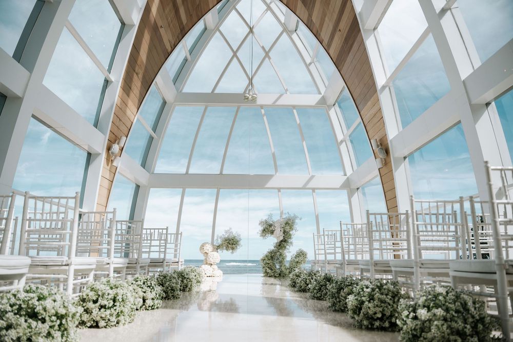 Panoramic view of a modern glass-roofed chapel interior with white beams and neutral decor for a wedding ceremony.