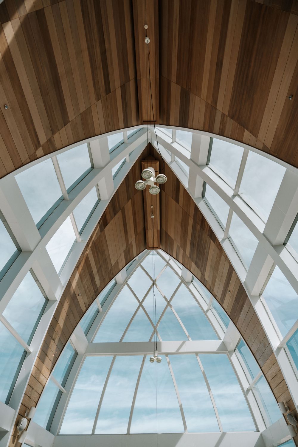 Contemporary wooden chapel ceiling with geometric skylights letting in natural light and blue sky views.