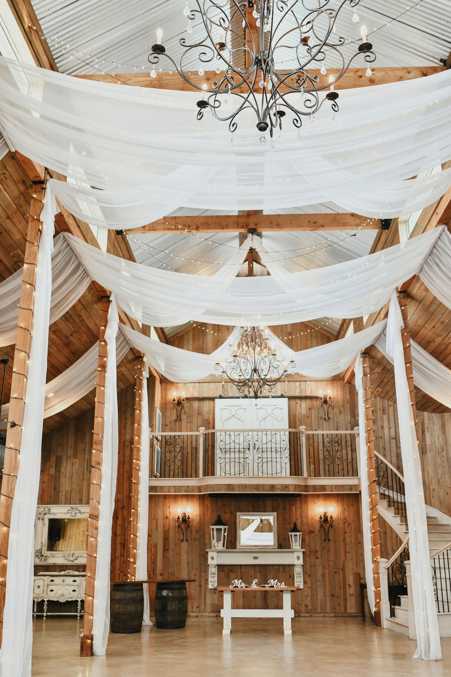 Dreamy rustic-modern barn with airy white drapery and open beams inside the whispering oaks wedding venue in valley view, tx