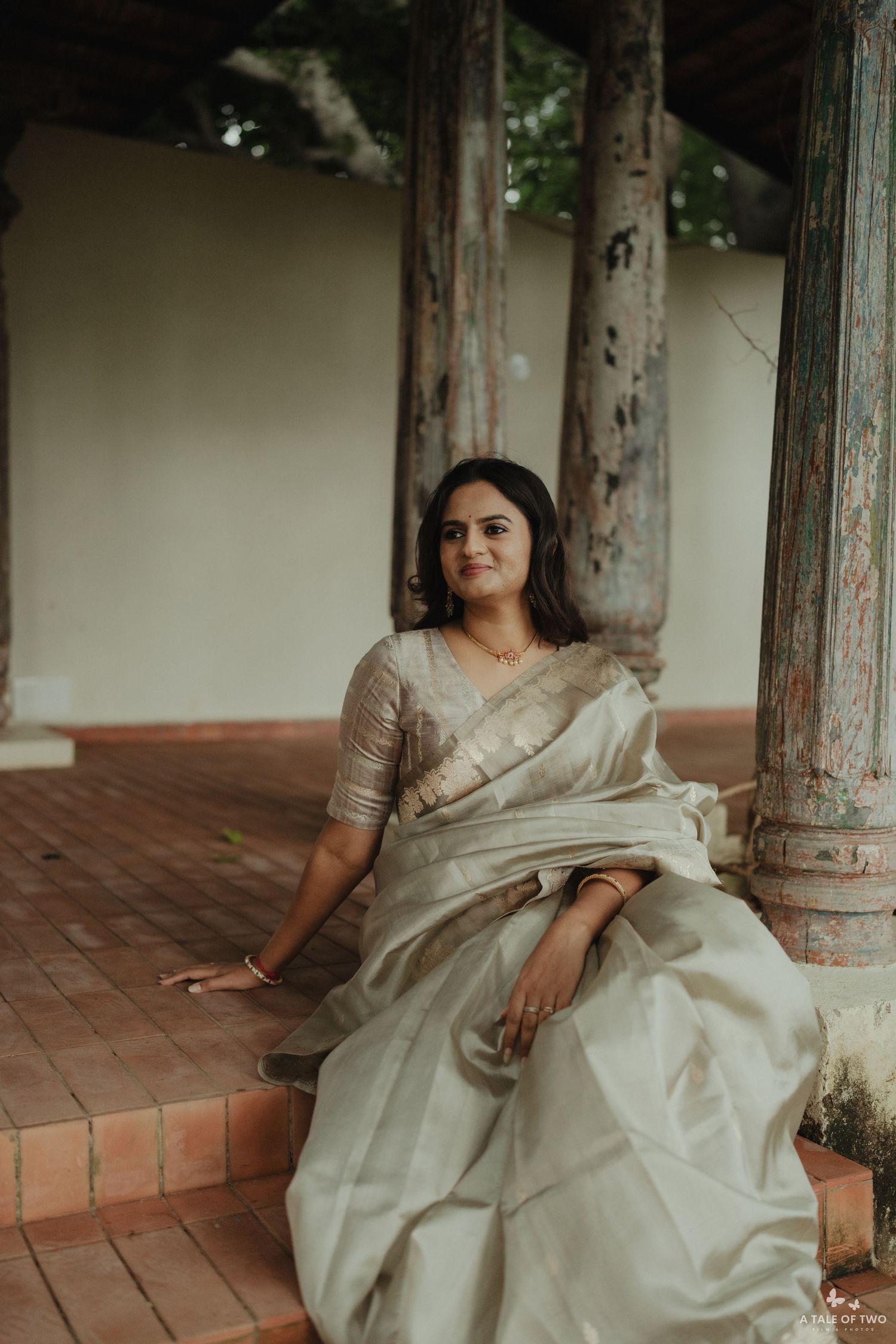 A person in a flowing white dress sits gracefully on a rustic porch with vintage pillars.