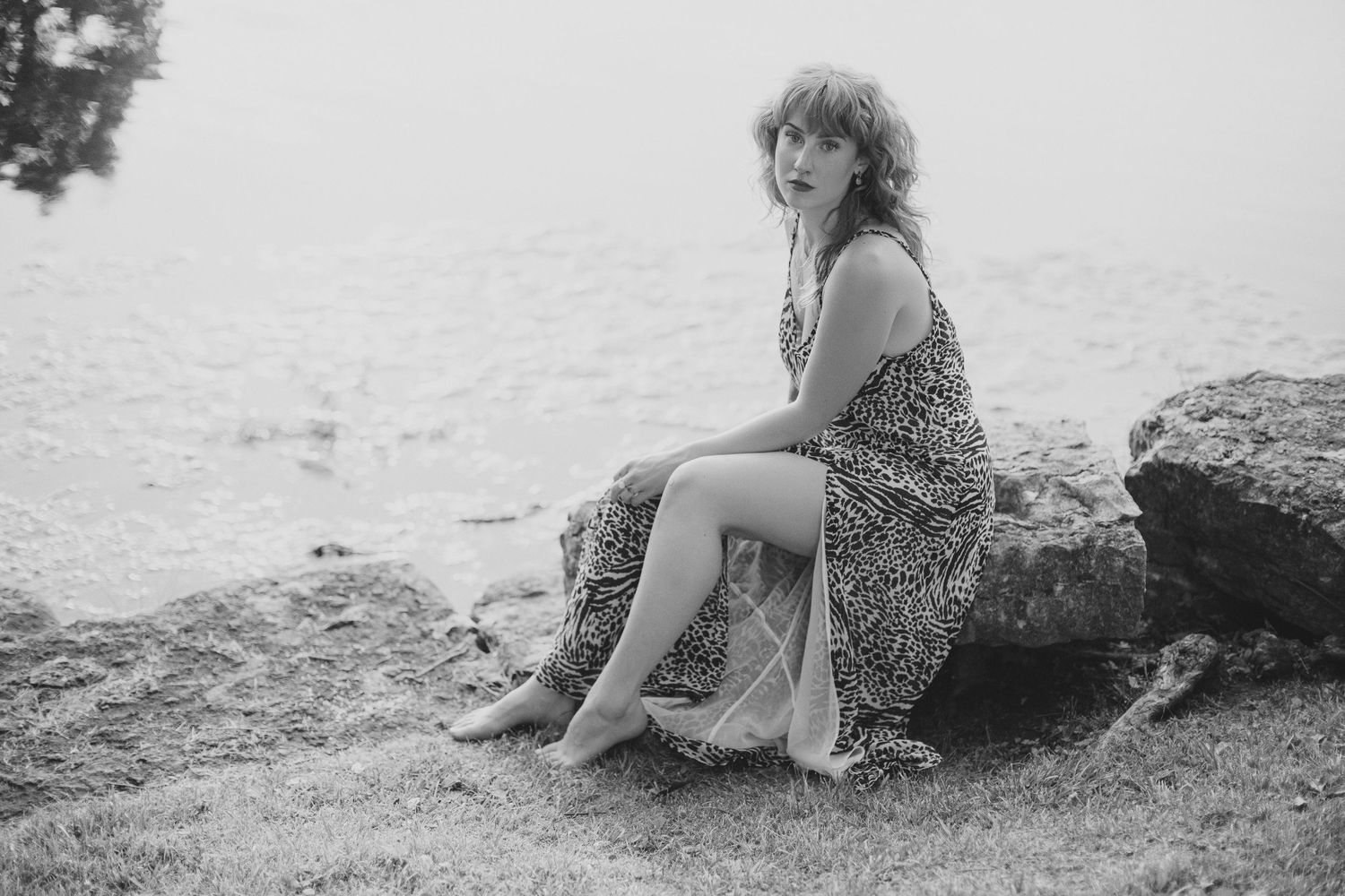 Black and white photo of someone sitting on coastal rocks in a flowing dress.