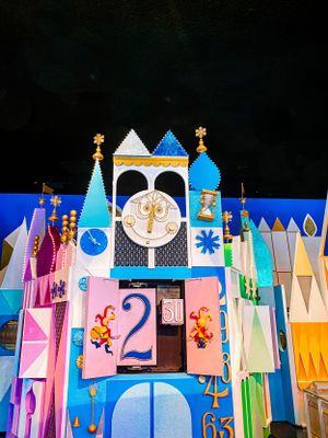 Colorful characters and geometric shapes from Disney's 'It's a Small World' attraction display against a dark background.