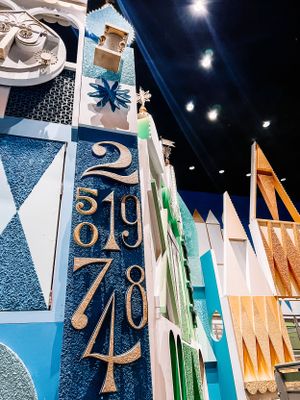 Colorful geometric wall art in blue, white and orange with metallic numbers displayed in an indoor exhibition space.